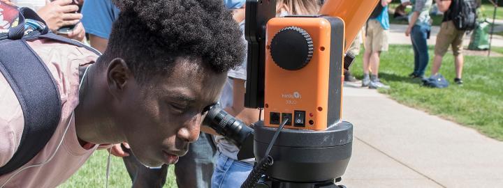 Student looks into a telescope at an eclipse party on campus.